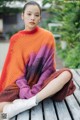 A woman sitting on a wooden bench wearing a colorful sweater.