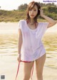 A woman in a white shirt and red bikini standing on a beach.