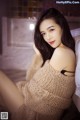 A woman in a beige sweater sitting on a bed.
