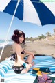 A woman in a bikini sitting under an umbrella on the beach.